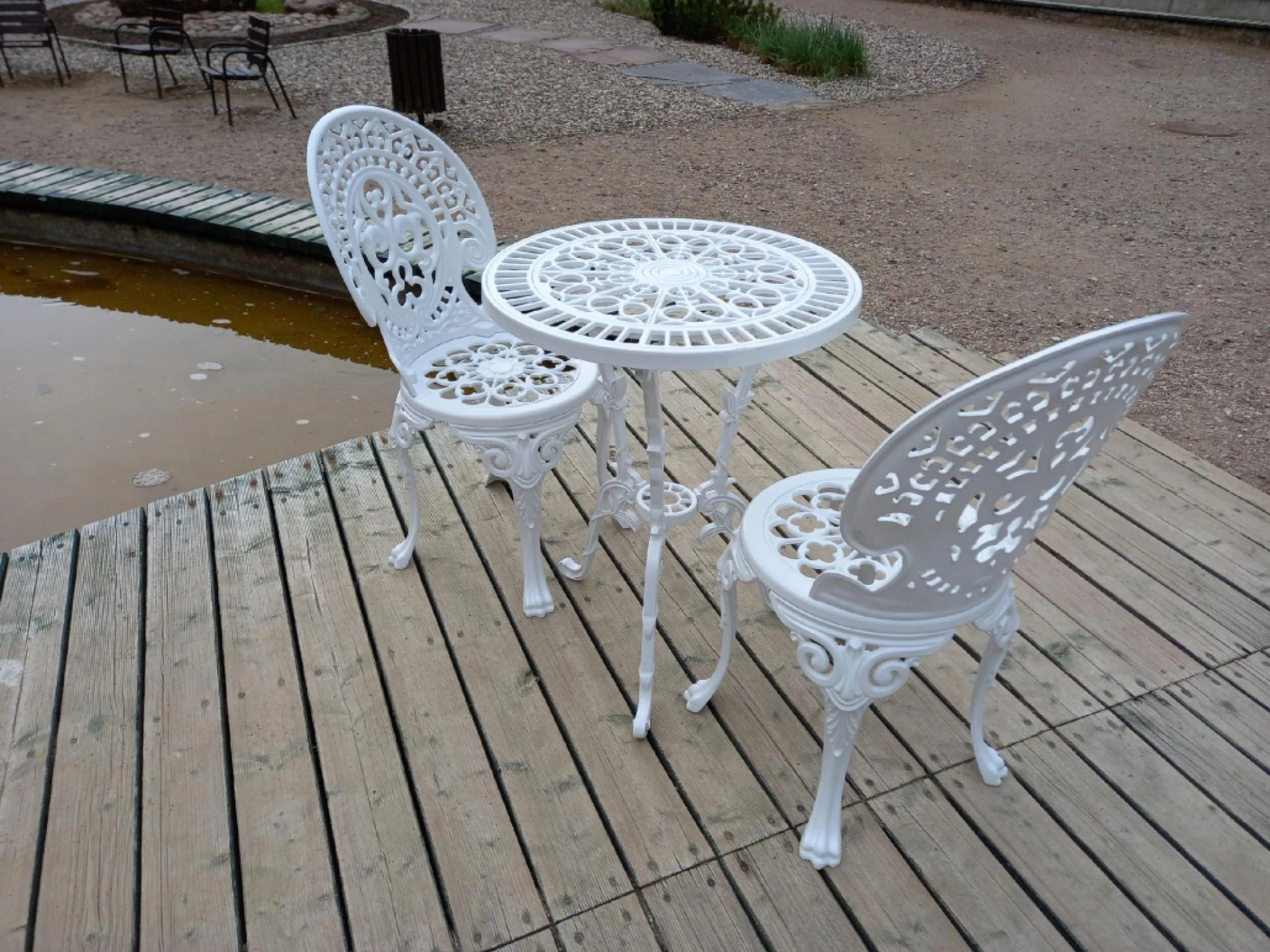 Weißes Romantic-Gartenmöbelset mit Tisch Ø 56,5 cm und zwei Stühlen auf einer Holzterrasse